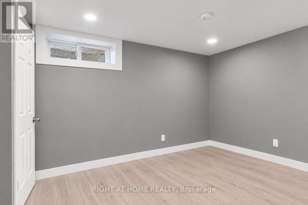Empty basement room with grey walls, light wood-look flooring, and a small window. - Basement - 200 Renfro Crescent, London South