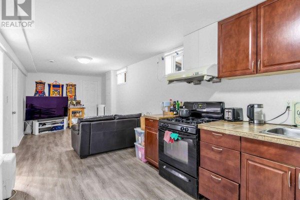 Basement with a dark leather sofa, television, and small kitchen area. - Basement - 210 Gowan Avenue, Toronto
