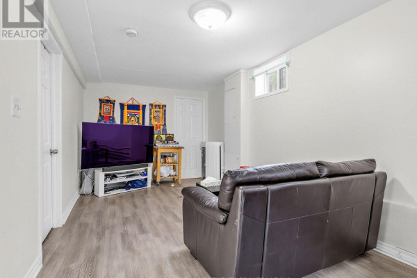 Living area in the basement with a dark leather sofa and television visible. - Basement - 210 Gowan Avenue, Toronto