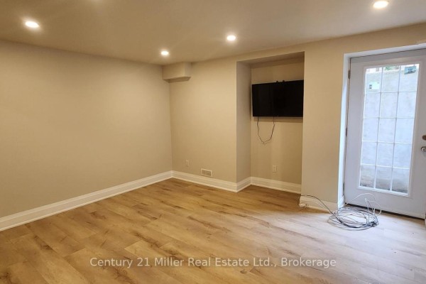 Basement room with light wood laminate flooring, neutral walls, wall-mounted television, and a glass door. - Basement - 2184 Winding Woods Drive, Oakville