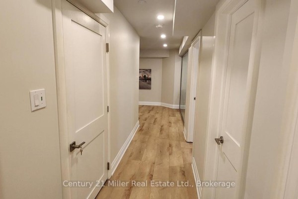Basement hallway with light wood laminate flooring, multiple white doors, and overhead lighting. - Basement - 2184 Winding Woods Drive, Oakville