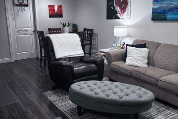A living area with a recliner, sofa, ottoman, and dining set, with artwork on the walls. - Basement - 2544 Pillette Road, Windsor