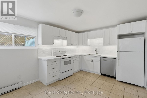White kitchen with white cabinets, stainless steel appliances, and beige tile flooring. - Basement - 255 Greenwood Avenue, Oshawa