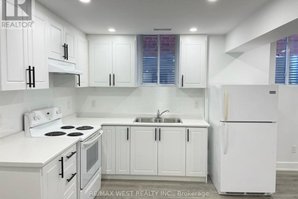 Basement kitchen with white cabinets, white countertops, white appliances, and a window. - Basement - 26 Smoothwater Street, Brampton