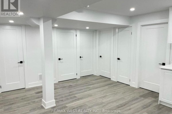 Hallway in a basement with white doors, black door handles, and light grey wood-look flooring. - Basement - 26 Smoothwater Street, Brampton