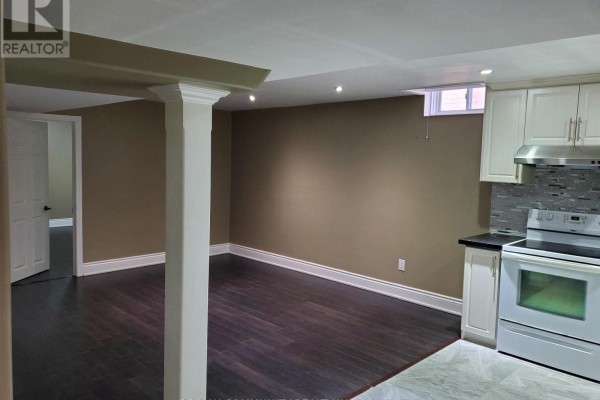 Basement living area with dark hardwood floors, beige walls, and a doorway leading to another room. - Basement - 27 Karen Miles Crescent, Markham