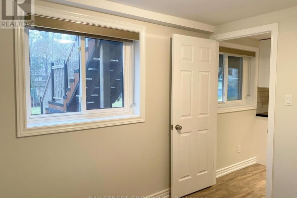 Basement hallway with two windows showing stairs and a partially open door revealing a kitchen. - Basement - 29 Carlton Road, Markham
