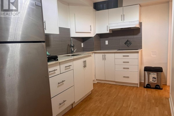 Compact basement kitchen with white cabinets, granite countertops, stainless steel appliances, and wood-look flooring. - Basement - 3156 Mccarron Crescent, Mississauga