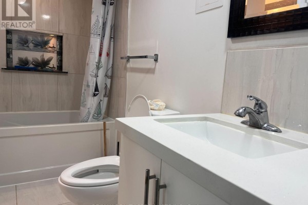 Basement bathroom featuring a white vanity, toilet, bathtub with a sailboat shower curtain, and tiled walls. - Basement - 3156 Mccarron Crescent, Mississauga