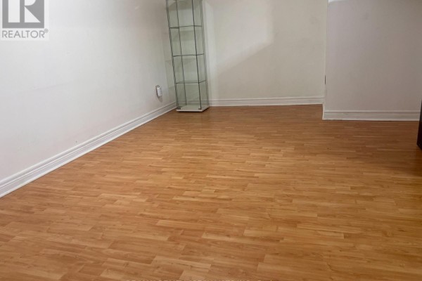 Empty basement room with white walls, light wood laminate flooring, and a glass display shelf. - Basement - 3156 Mccarron Crescent, Mississauga