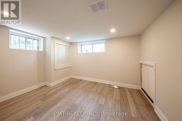 Empty basement room with light wood laminate flooring, two windows, and a bi-fold door closet. - Basement - 34 Robindale Avenue, Toronto