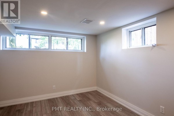Unfurnished basement room with light wood laminate flooring and three horizontal windows providing natural light. - Basement - 34 Robindale Avenue, Toronto