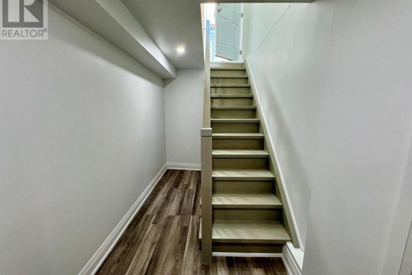 Interior view of a narrow staircase with light grey walls, wood-look flooring, and a partially open door. - Basement - 375 Wilfred Murison Avenue, Markham