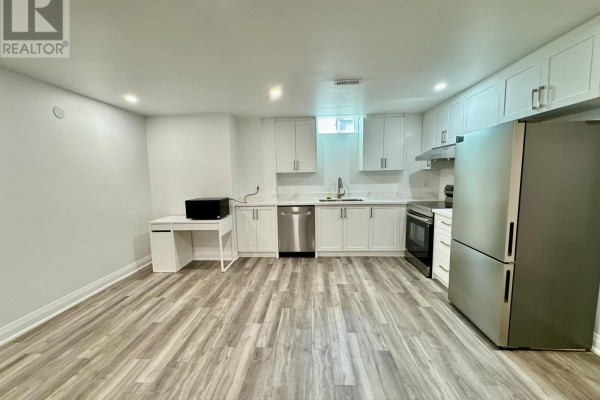A basement kitchen with white cabinets, stainless steel appliances, a small desk, and light wood-look flooring. - Basement - 375 Wilfred Murison Avenue, Markham