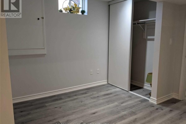 Basement bedroom with grey laminate flooring, white trim, and a sliding closet door. - Basement - 39 Wood Rim Drive, Richmond Hill