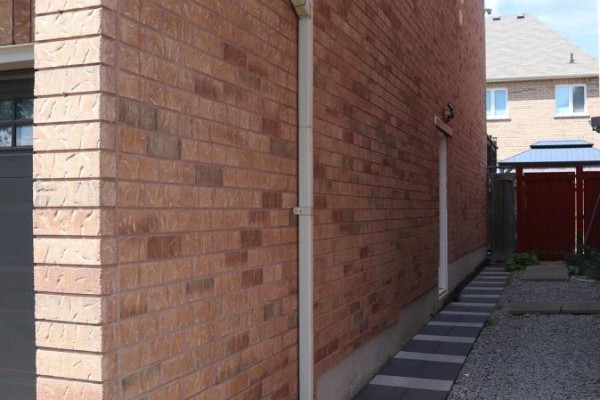 Side view of brick house exterior with a concrete walkway and fenced backyard visible. - Basement - 4 Elliottglen Drive, Ajax