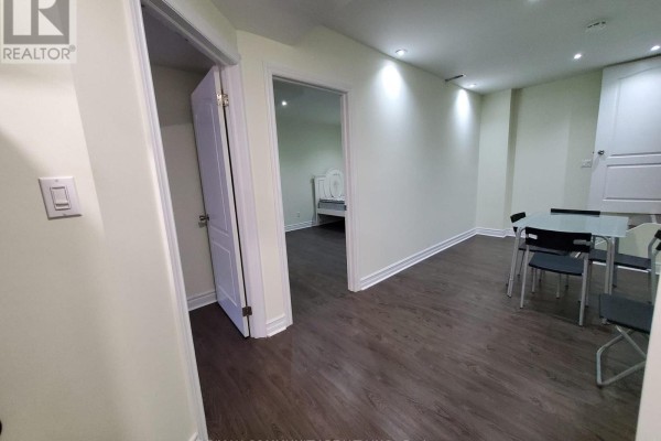 Basement living area with dark wood floors, dining table, and view into a bedroom. - Basement - 4 Elliottglen Drive, Ajax