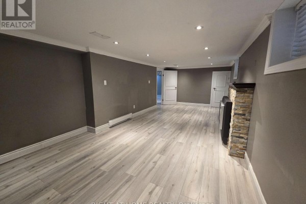 Basement living area with a fireplace, doors, and heating vents, featuring gray walls and light wood floors. - Basement - 46 Haverson Boulevard, Toronto