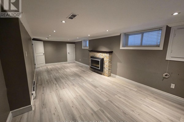 Basement living space with wood laminate floors, a fireplace, and two doors opening to adjacent areas. - Basement - 46 Haverson Boulevard, Toronto