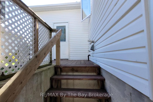 Wooden stairs leading down from a deck to a concrete foundation and a basement door. - Basement - 48 Caribou Trail, Wasaga Beach