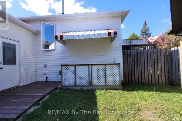Wooden deck with white lattice skirting and a red and white striped awning on the side of a house. - Basement - 48 Caribou Trail, Wasaga Beach