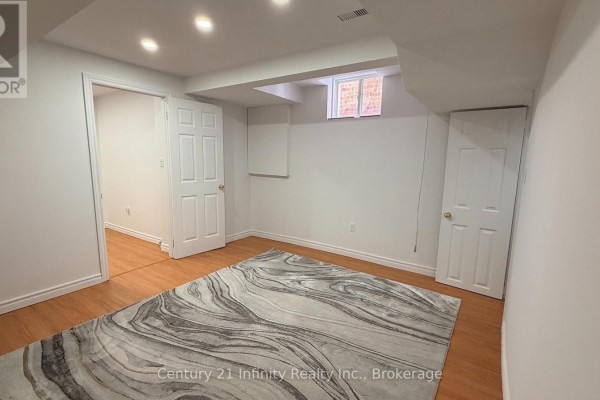 Basement room with white walls, wood floor, large abstract rug, and two doorways. - Basement - 5 Dusk Owl Drive, Toronto