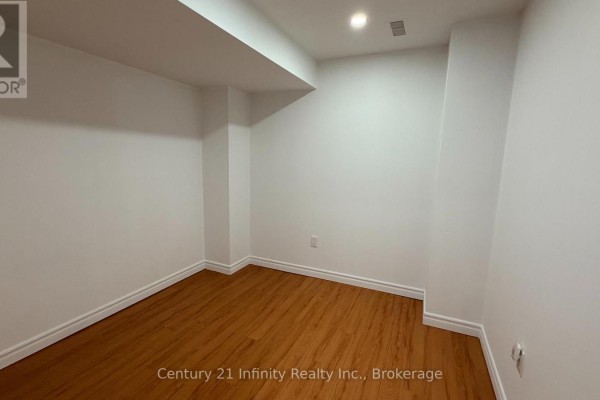 Empty basement room with white walls, wood flooring, and a large support column. - Basement - 5 Dusk Owl Drive, Toronto
