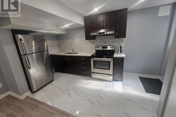 A basement kitchen with dark wood cabinets, white countertops, and stainless steel refrigerator. - Basement - 5 Watson Drive, New Tecumseth