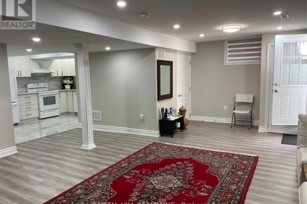 Finished basement with gray walls, light wood floors, a white kitchen, and red Persian rug. - Basement - 51 Glenthorne Drive, Toronto