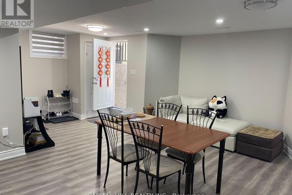 Finished basement with a dining table, white couch, and a door leading outside. - Basement - 51 Glenthorne Drive, Toronto