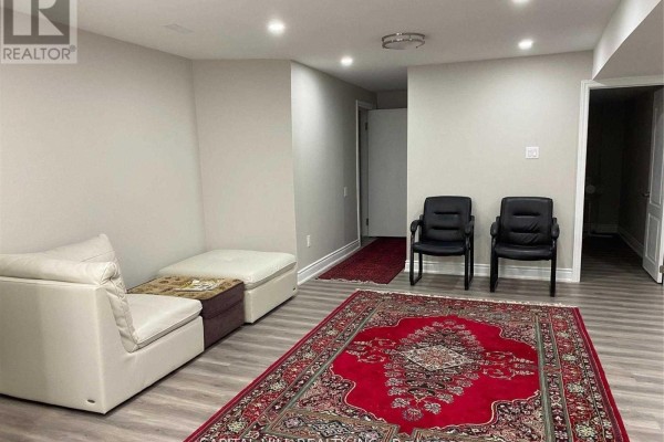 Finished basement with a red Persian rug, white sectional couch, and two black office chairs. - Basement - 51 Glenthorne Drive, Toronto