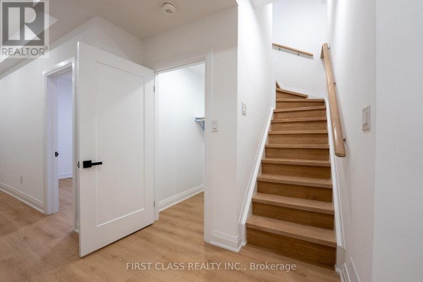 Basement hallway with light wood laminate flooring, a white staircase with wooden steps, and multiple interior doors. - Basement - 544 White's Hill Avenue, Markham