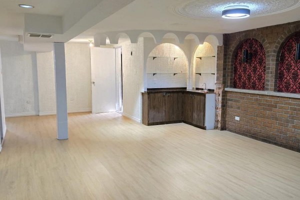 Basement recreation room with wood-look flooring, wet bar, arched shelving, and brick wall. - Basement - 61 Hardwick Court, Toronto