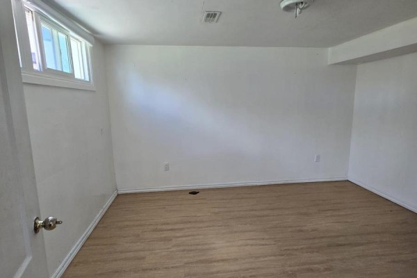 Empty basement room with white walls, wood-look flooring, and a small window. - Basement - 61 Hardwick Court, Toronto