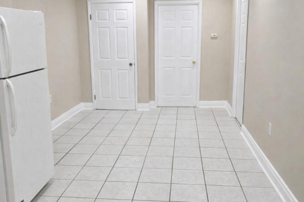 Basement area with white refrigerator, two white doors, and beige walls on tiled floor. - Basement - 621 Dixon Road, Toronto