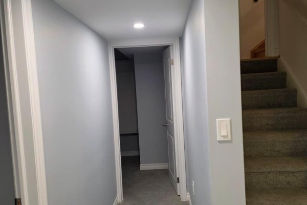Hallway with light grey walls and doors, featuring a carpeted staircase on the right. - Basement - 63 English Drive E, New Tecumseth