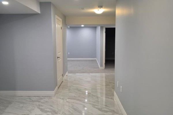 Hallway with marble-look tile flooring and light grey walls, leading to unfinished rooms. - Basement - 63 English Drive E, New Tecumseth