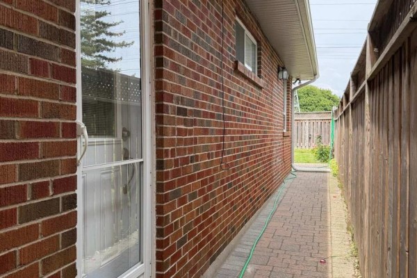 Exterior view of brick house with wooden fence and paved pathway. - Basement - 65 Glen Agar Drive, Toronto