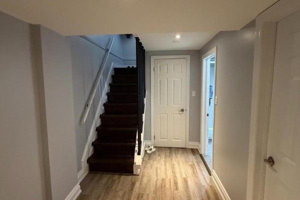 Basement hallway with wood-look laminate flooring and staircase to upper level. - Basement - 65 Glen Agar Drive, Toronto