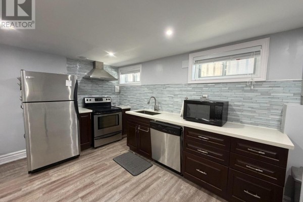 Kitchen with stainless steel appliances, dark wood cabinets, and light backsplash. - Basement - 65 Glen Agar Drive, Toronto