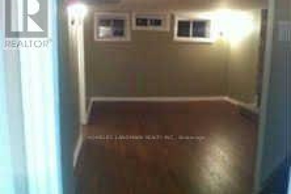Empty basement room with wood floors, olive green walls, and two small windows. - Basement - 7080 Estoril Road, Mississauga