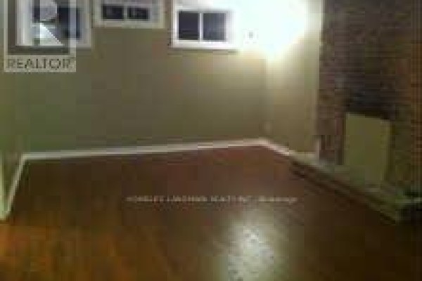 Basement room with wood floors, olive green walls, a brick fireplace, and two windows. - Basement - 7080 Estoril Road, Mississauga