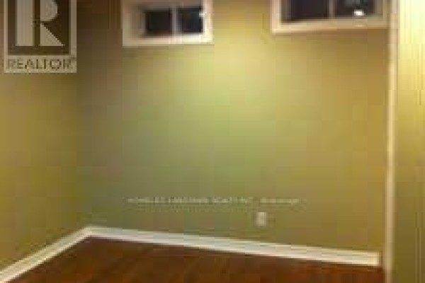 Corner of a basement room with wood floors, light green walls, and a small window. - Basement - 7080 Estoril Road, Mississauga