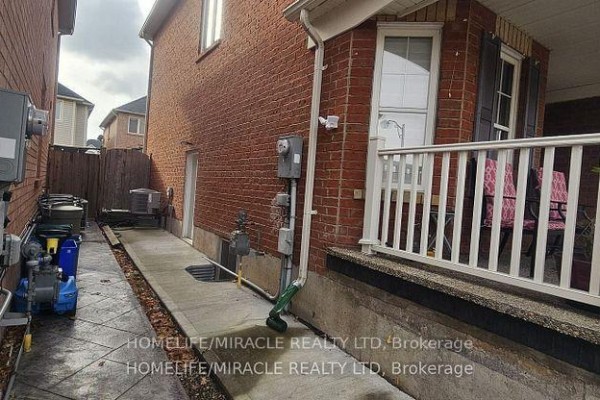 Side view of the house showing a narrow concrete walkway, exposed utility meters, and a fence. - Basement - 718 Speyer Circle, Milton