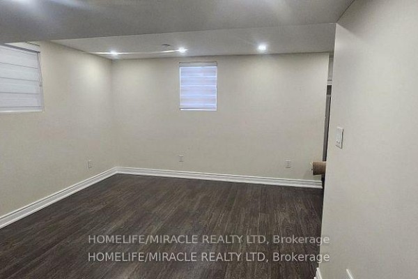 Unfurnished basement room with dark wood laminate flooring, white baseboards, and two small windows. - Basement - 718 Speyer Circle, Milton