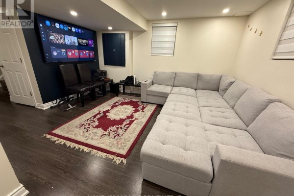 Basement living area with a large sectional sofa, red patterned rug, and a wall-mounted television. - Basement - 718 Speyer Circle, Milton