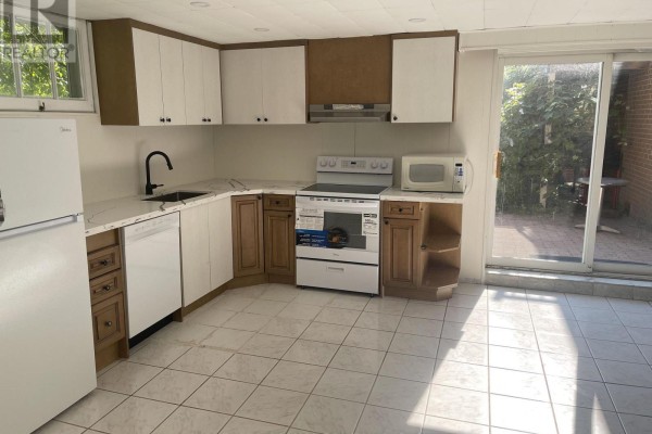 A basement kitchen features white and brown cabinets, a white refrigerator, dishwasher, stove, and microwave. - Basement - 74 Valentine Drive, Toronto