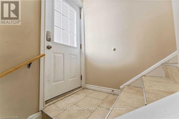 Exterior basement door with glass panes, tiled floor, and wood handrail on stairs. - Basement - 864 Upper Ottawa Street, Hamilton