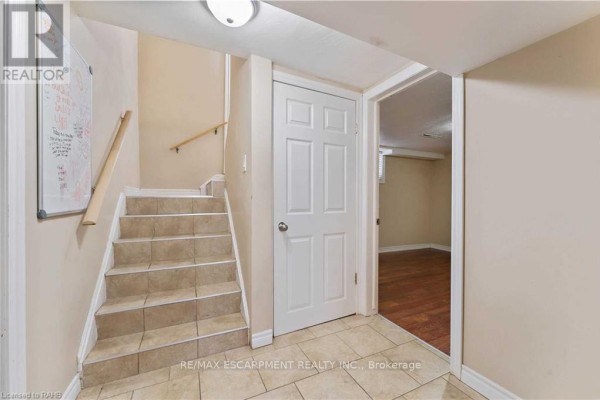 Staircase leading down to basement with tiled steps, wood handrail, and interior door. - Basement - 864 Upper Ottawa Street, Hamilton