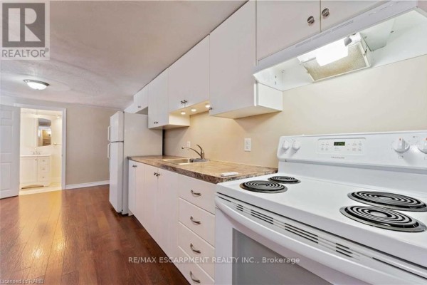 Spacious basement rec room with wood floors, two windows with blinds, and a small kitchen area. - Basement - 864 Upper Ottawa Street, Hamilton